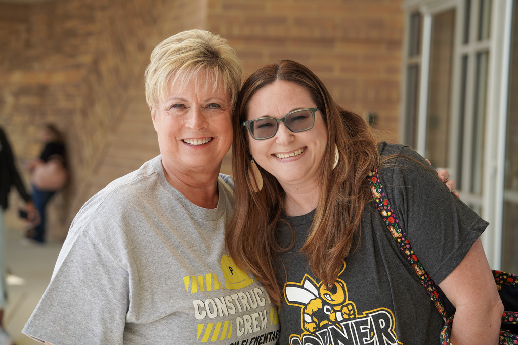 Two women stand together for a photo outside a building.