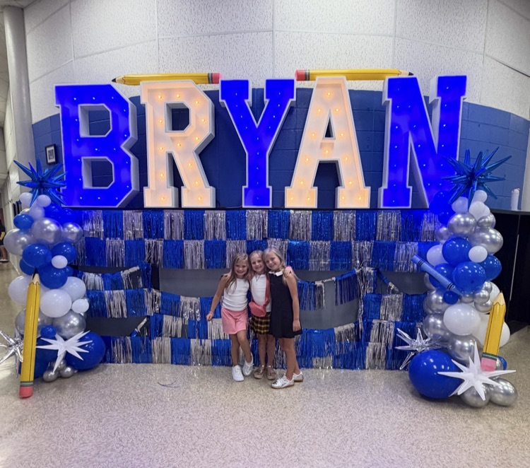 Three girls standing as friends in front of a Bryan sign