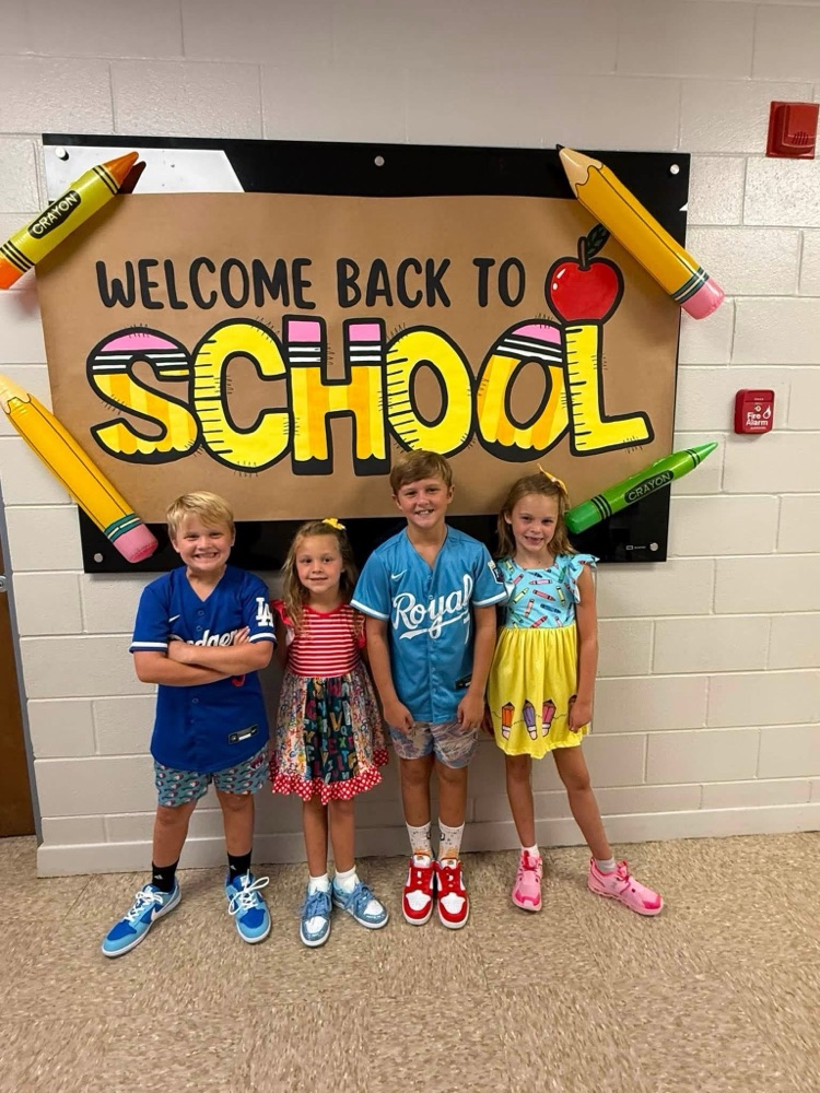 four students posing in front of a welcome back to school poster