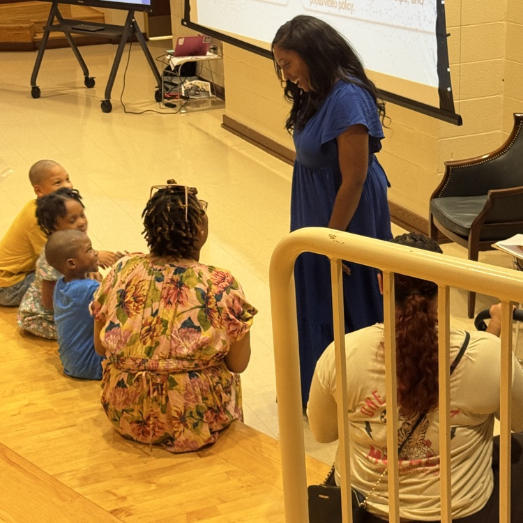 Teacher standing and talking to a parent with three children sitting and listening 