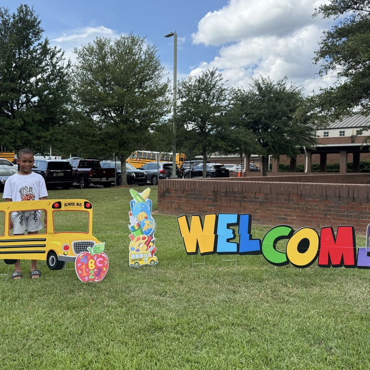 child standing behind a cut out display of a school bus with the word WELCOME in colorful letters