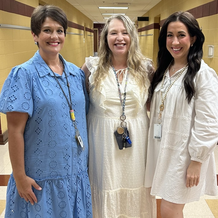 three teachers standing close together in the school hall 