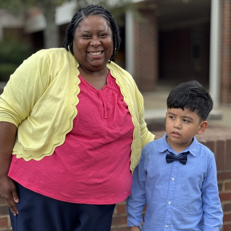a teacher and a student standing close together outside of the school