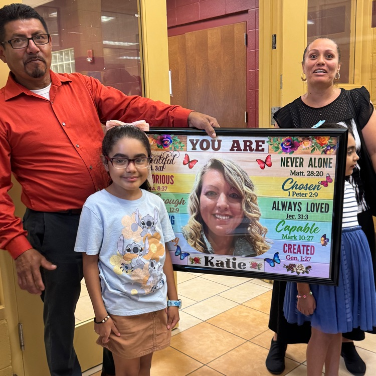 a dad, mom, and two daughters holding a framed picture of their new teacher