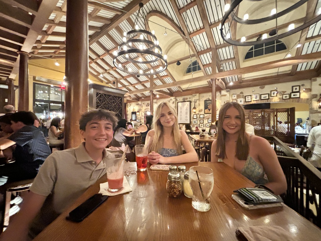 Two girls and a boy sitting at a table in a restaurant and smiling.