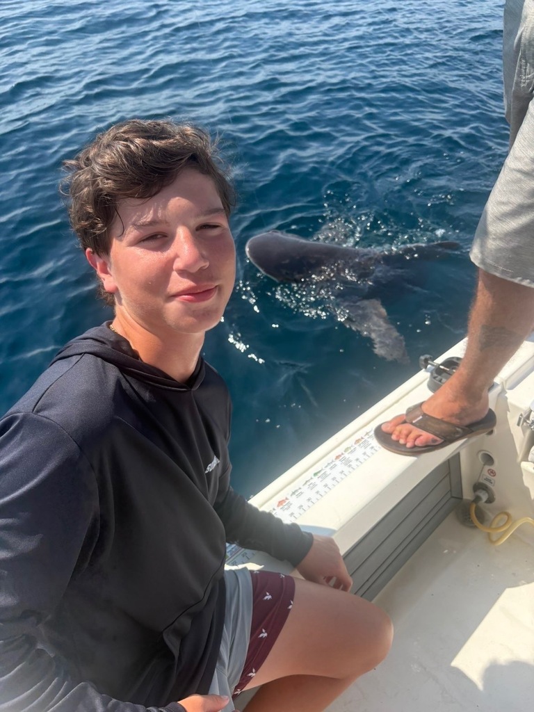 A boy poses next to a shark while on a boat in the ocean.