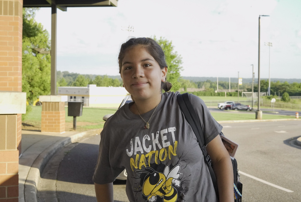 A girl smiles while standing outside a school.