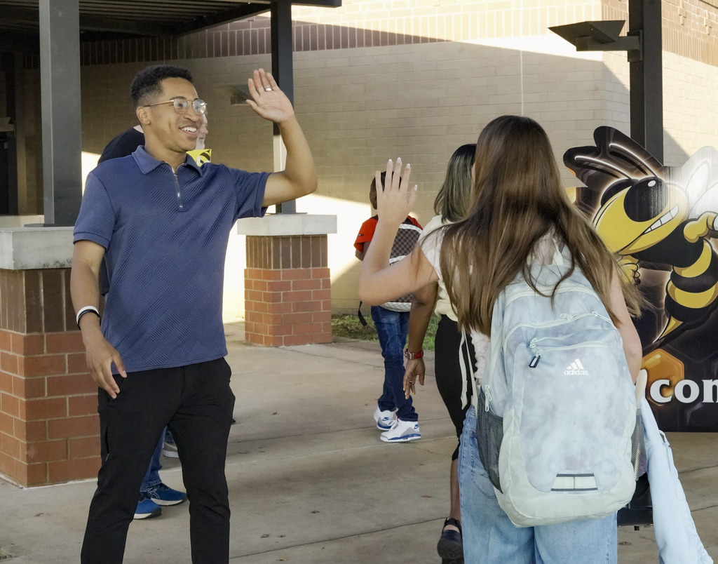 A man gives a student a high-five as they stand outside a school.