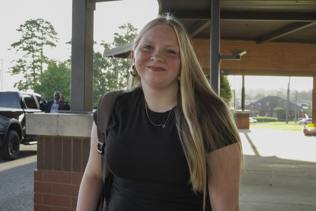 A girl stands outside a school and smiles.