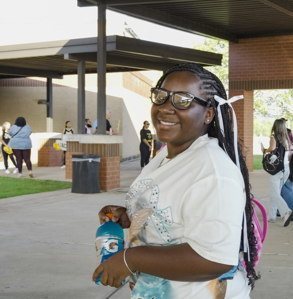 A girl smiles while standing outside a school.