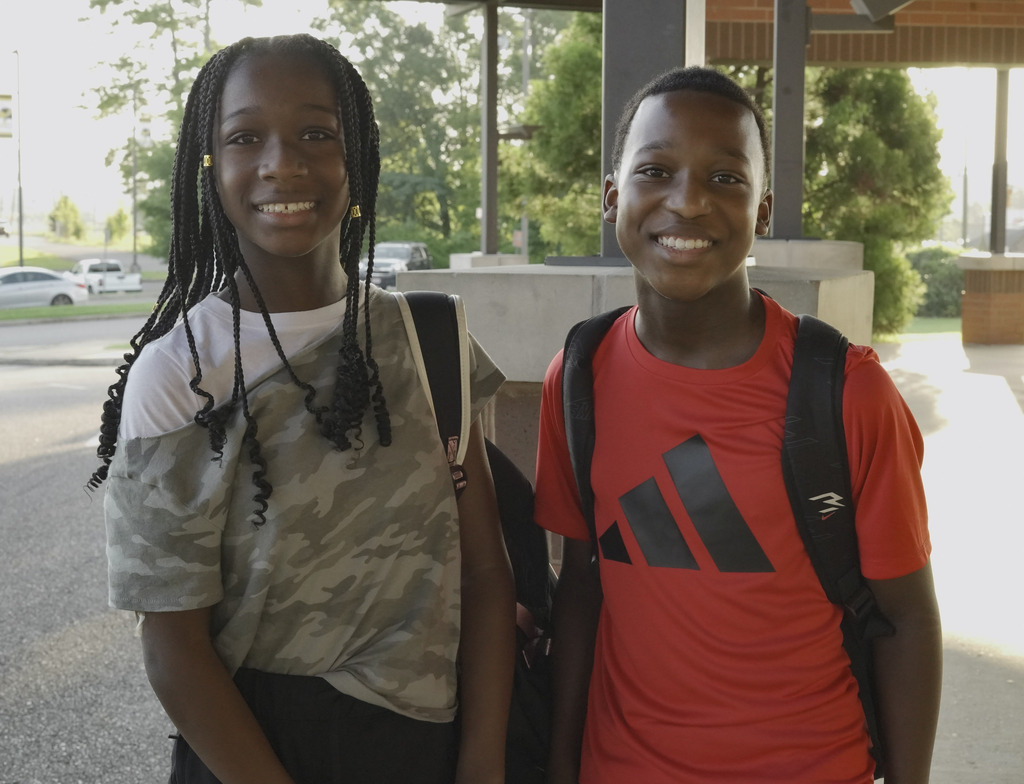 Two children stand outdoors and smile for a photo.