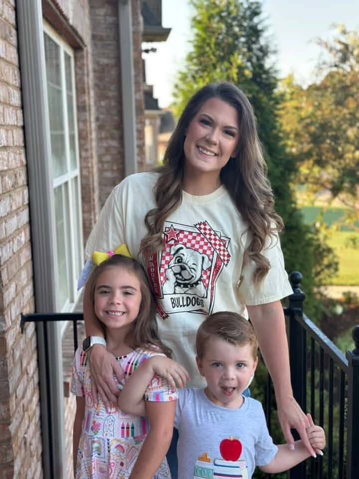 A woman and two children pose for a photo on a balcony outside a house.