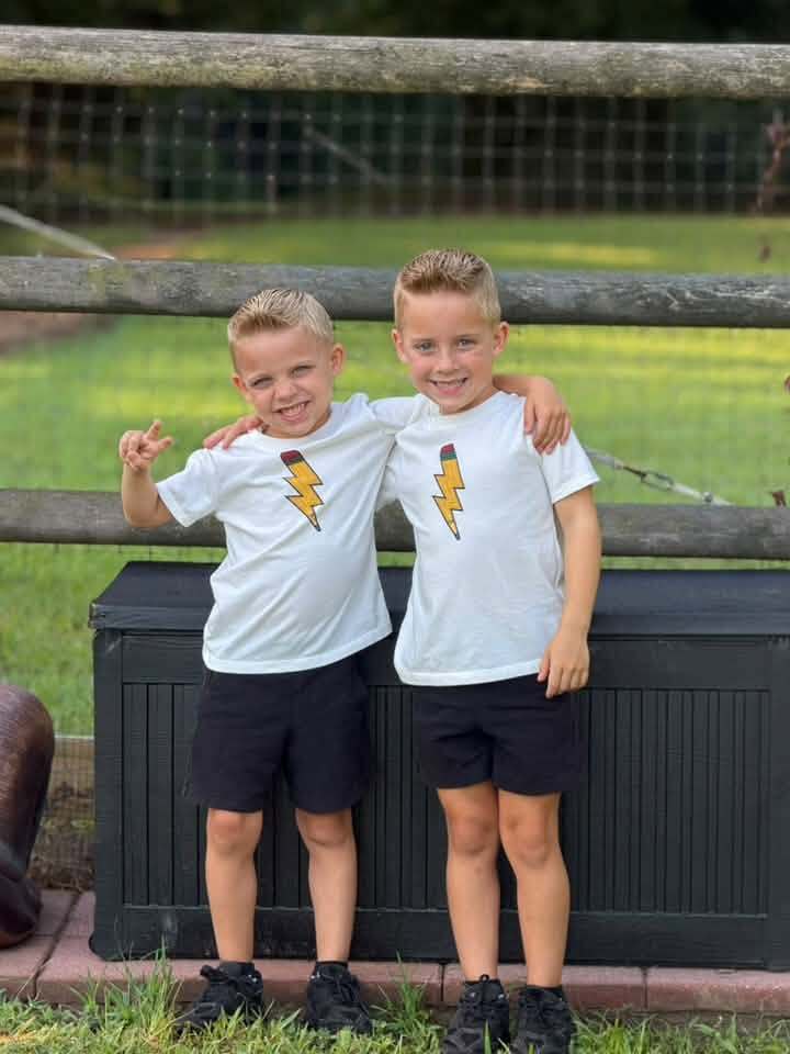 Two boys wearing matching outfits stand outdoors and smile for a photo.