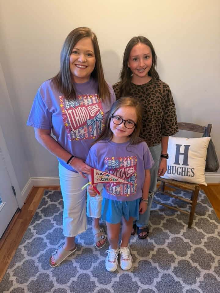 A woman and two children smile for a photo inside a room.