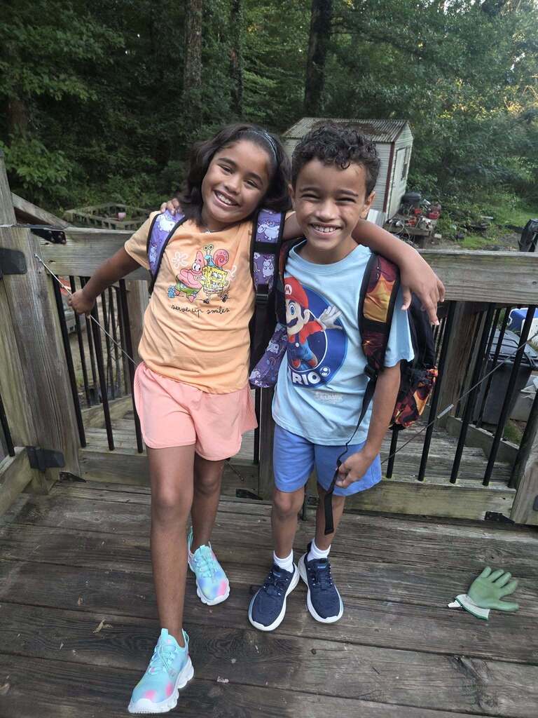 Children wearing backpacks smile and pose for a photo outdoors.