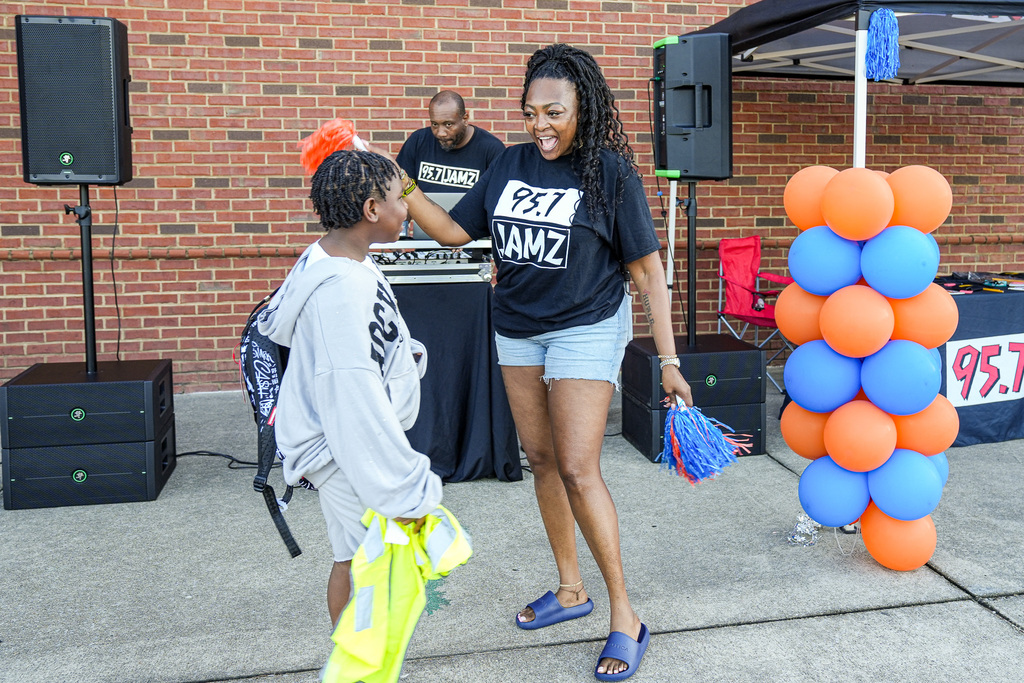 An employee from 95.7 JAMZ radio station waves pom poms and welcomes a student to school on the first day at Fultondale Elementary.