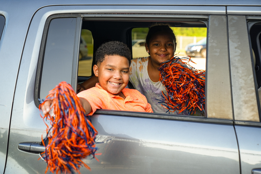 Two students sitting in the rear seat of a vehicle hold up pom poms and smile for the camera on the first day of school at Fultondale Elementary.