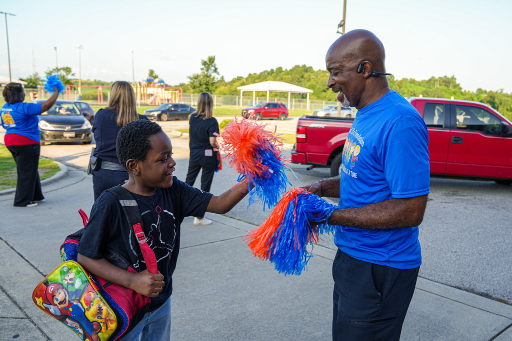 An employee welcomes a student to the first day of school at Fultondale Elementary with orange and blue pom poms.