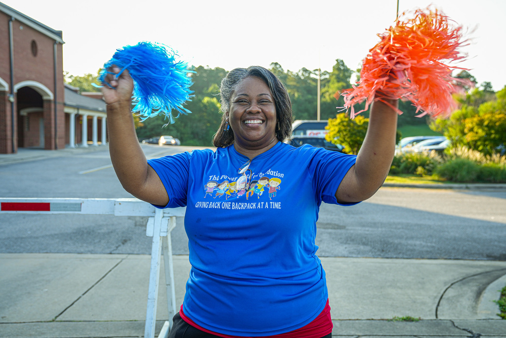 An employee at Fultondale Elementary waves orange and blue pom poms above her head on the first day of school.