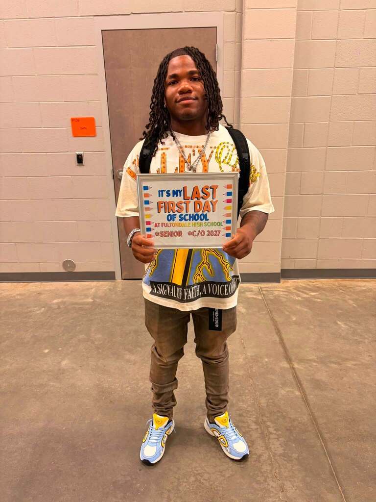 A Fultondale High School student stands for a photo in a school hallway. He holds up a sign that says "It's my last first day of school."