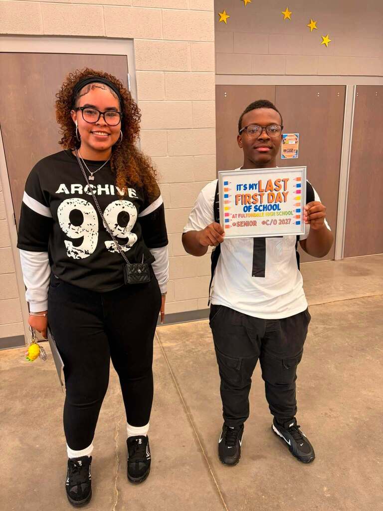 Two Fultondale High School seniors pose for a photo in a school hallway. One of the students holds up a sign that says "It's my last first day of school."