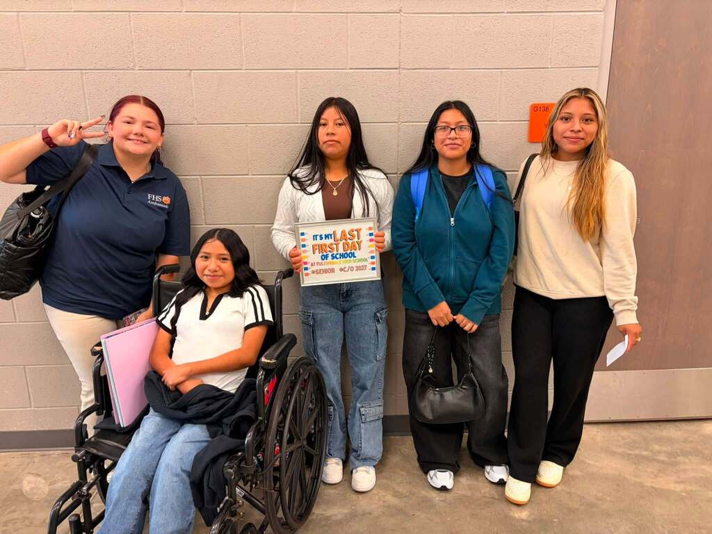 Fultondale High School students pose for a photo in a school hallway. On student holds up a sign that says "It's my last first day of school."