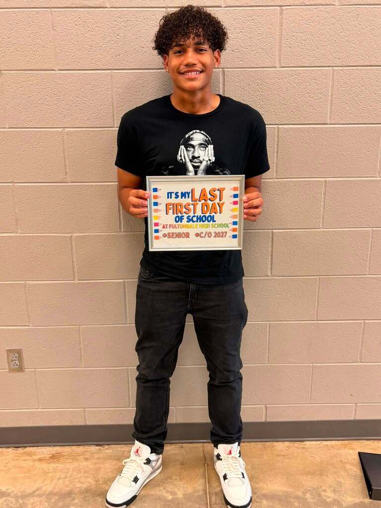 A Fultondale High School student poses for a photo in a school hallway. He holds up a sign that says "It's my last first day of school."