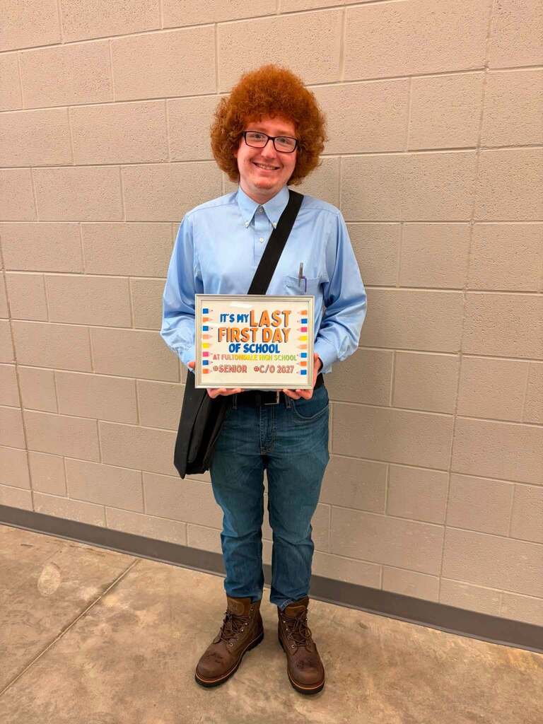 A Fultondale High School student poses for a photo in a school hallway. The student holds up a sign that says "It's my last first day of school."