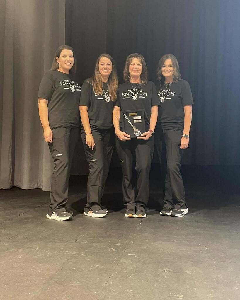 Women stand on a stage an smile for a photo. One of the women holds an award in her hands.