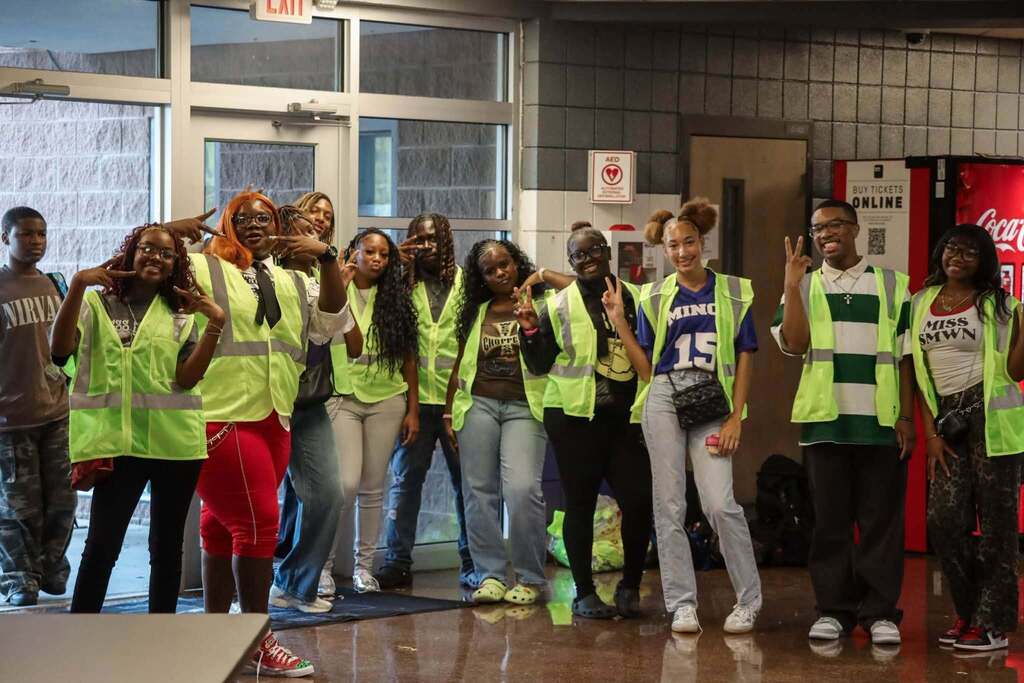 Students wearing yellow vests stand in the lobby of a school.