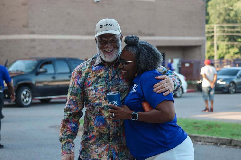 A man and a woman hug each other while standing outside a school.