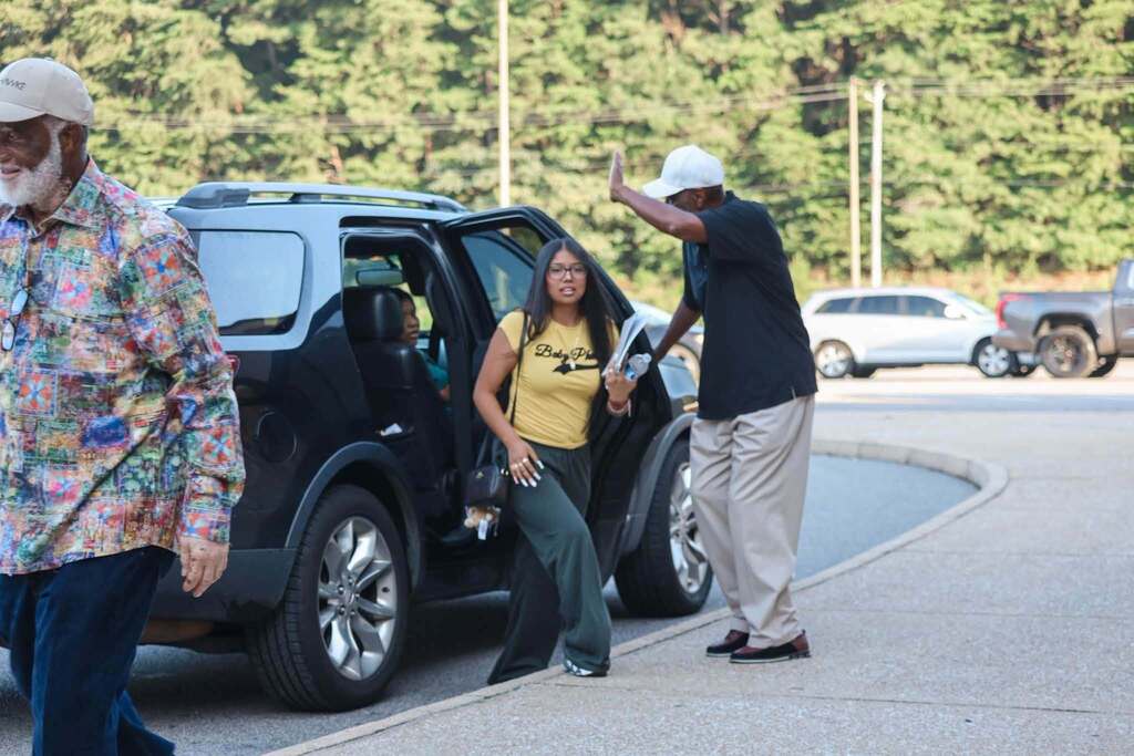 A man closes a car door as a student exits the car.