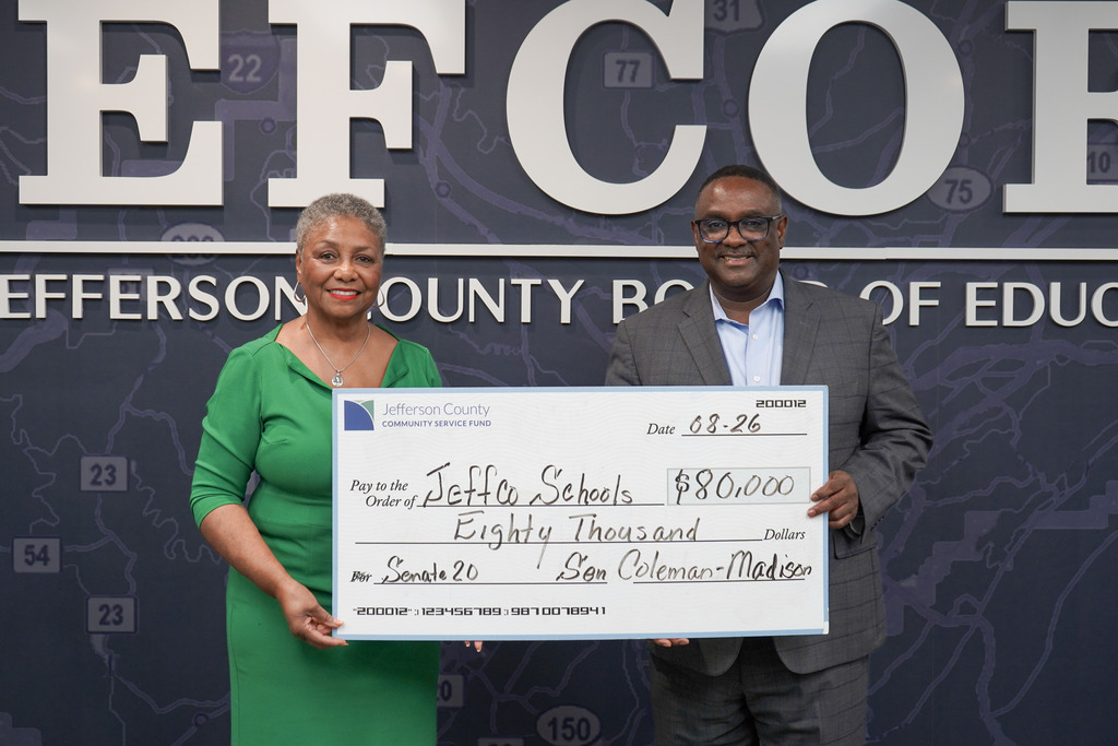 Senator Coleman-Madison and Superintendent Dr. Walter Gonsoulin smile for a photo in the JEFCOED conference room. They both hold a large check for $80,000.