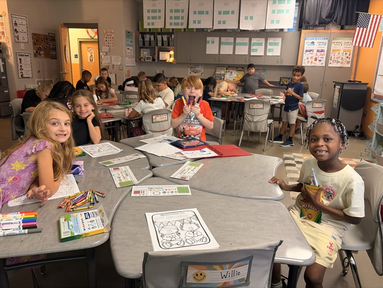 four students sitting at their desks smiling at the camera 