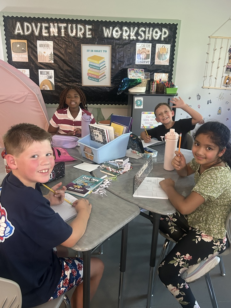 four students writing in their journals smiling at the camera 