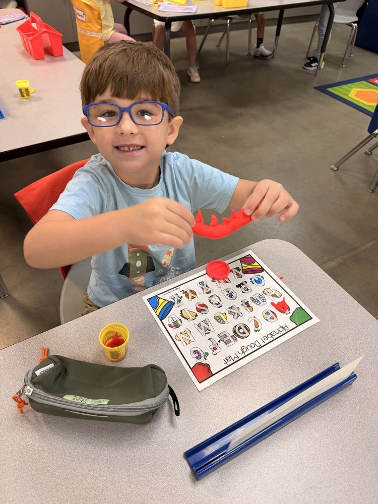boy sitting at his desk holding up his playdoh snake 