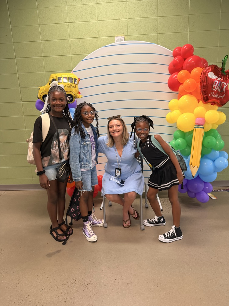 the students and a teacher posing in front of a notebook pattern backdrop with rainbow balloons 