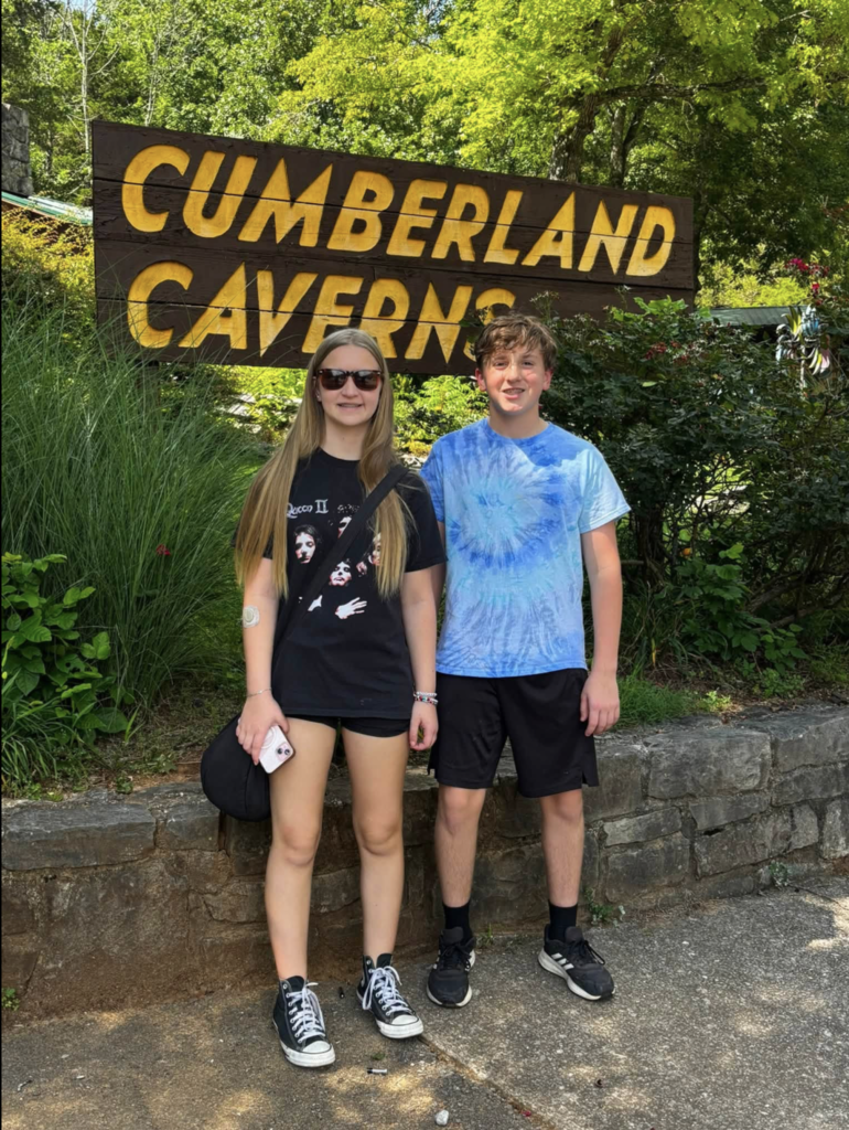 Two children stand in front of a sign that says Cumberland Caverns and smile for a photo.