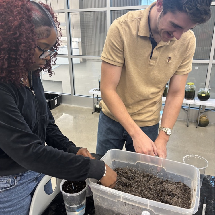 Two students working with soil in a bucket around the science table.
