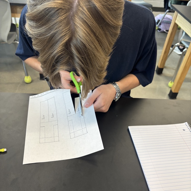 1 student using scissors to cut out a whirligig paper helicopter.