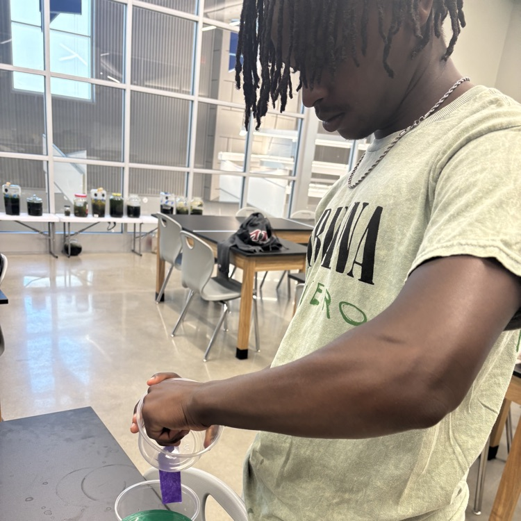 one student holding a clear plastic container around a black lab table.