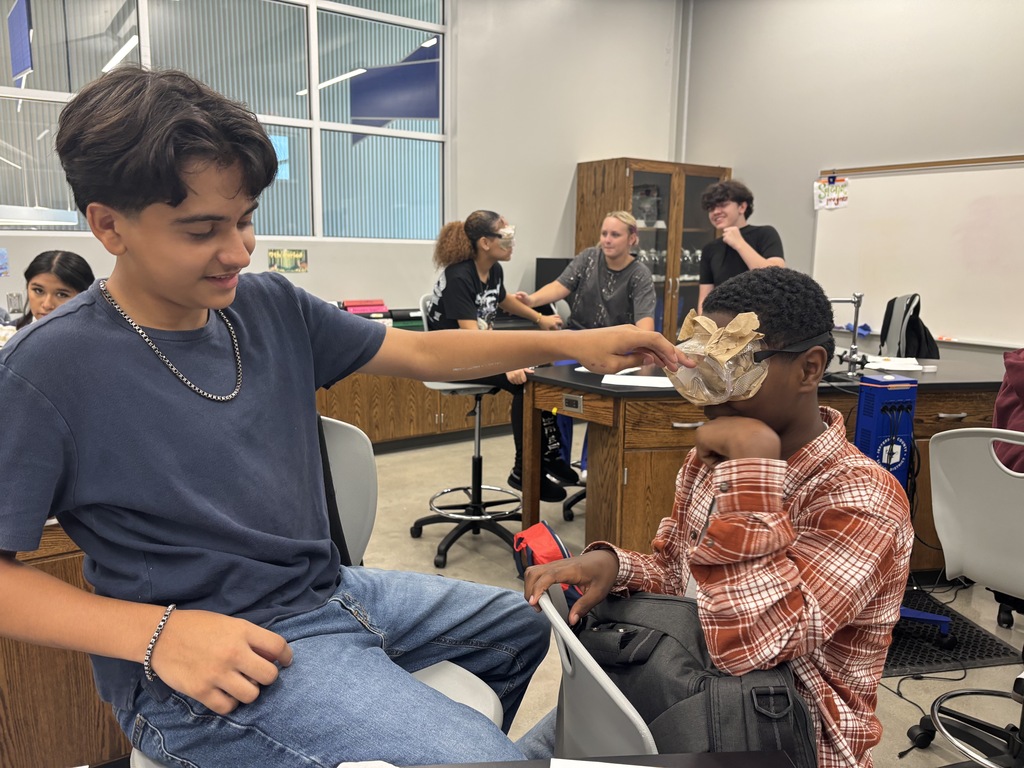 Two students in the lab. One student is wearing goggles that have been cover to block their vision and the other student poking his finger into the goggle to check the first student's vision.