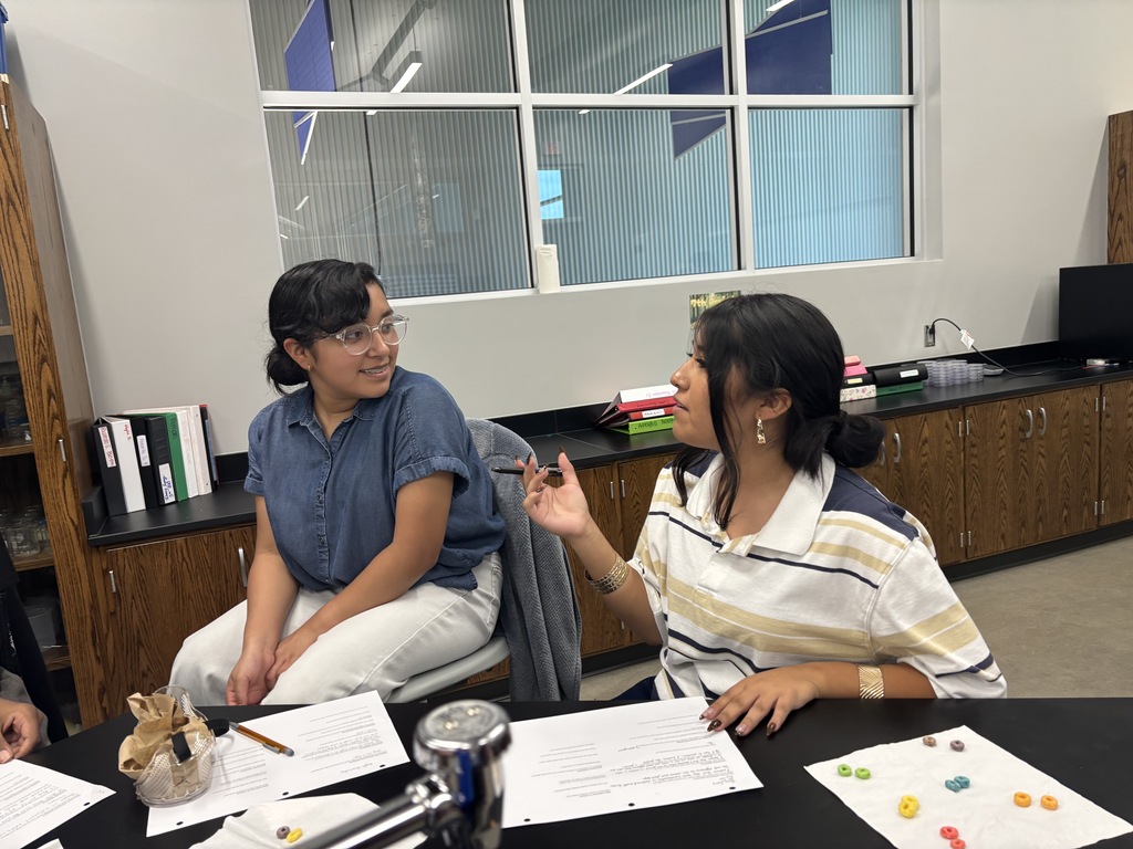 Two students sitting at a science lab table discussing the results of their science activity .