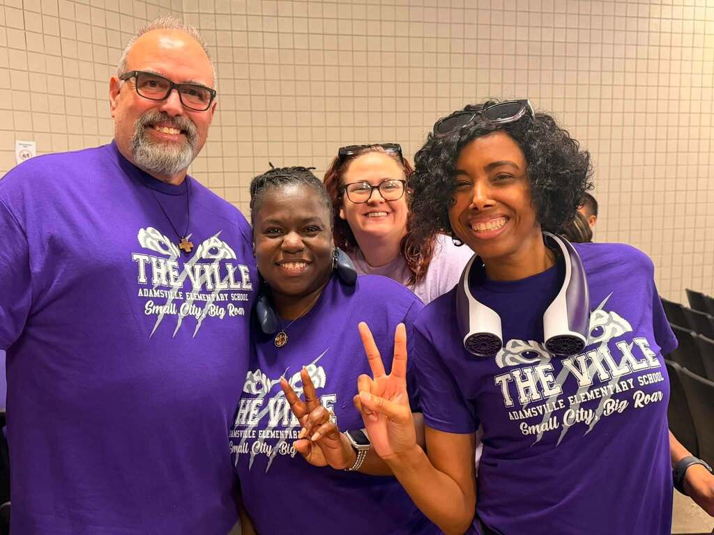 A group of people wearing matching Adamsville Elementary School shirts pose for a photo.