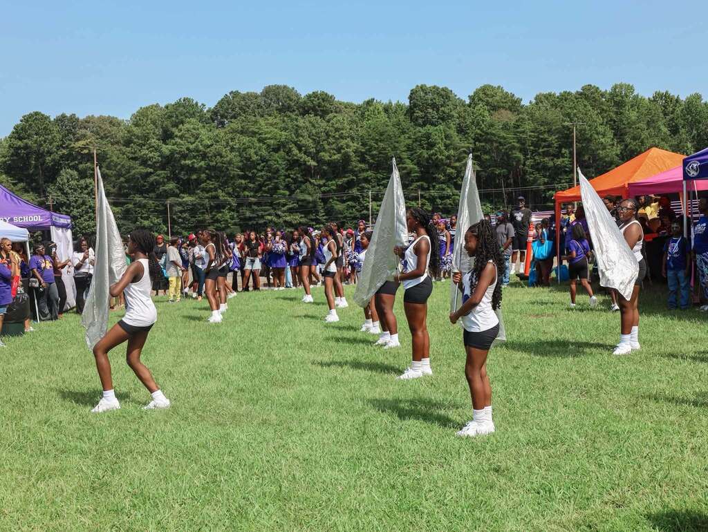 Students hold color guard flags and perform outdoors.