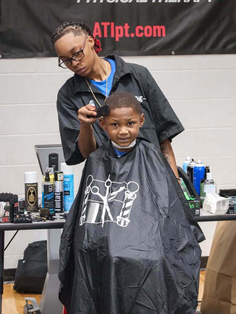 A child sits in a chair in a room and receives a hair cut.