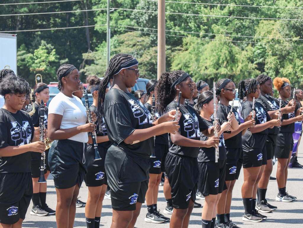 Band members stand outdoors and hold instruments during a performance.