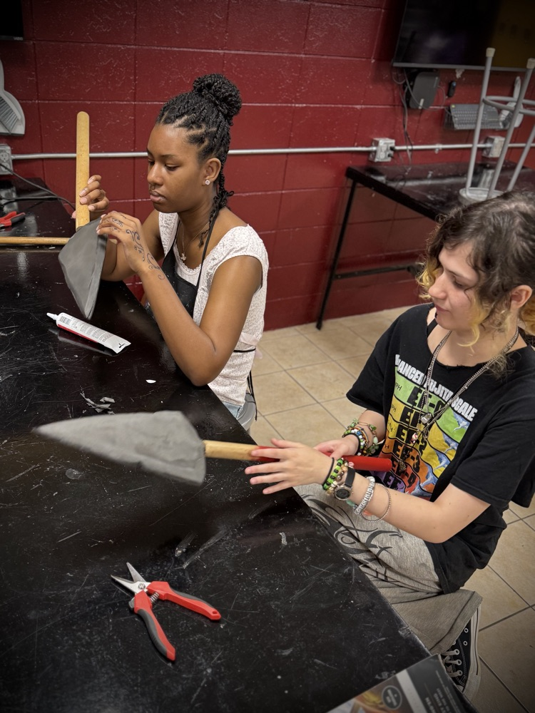 two students work on sanding and painting the poles of their spears