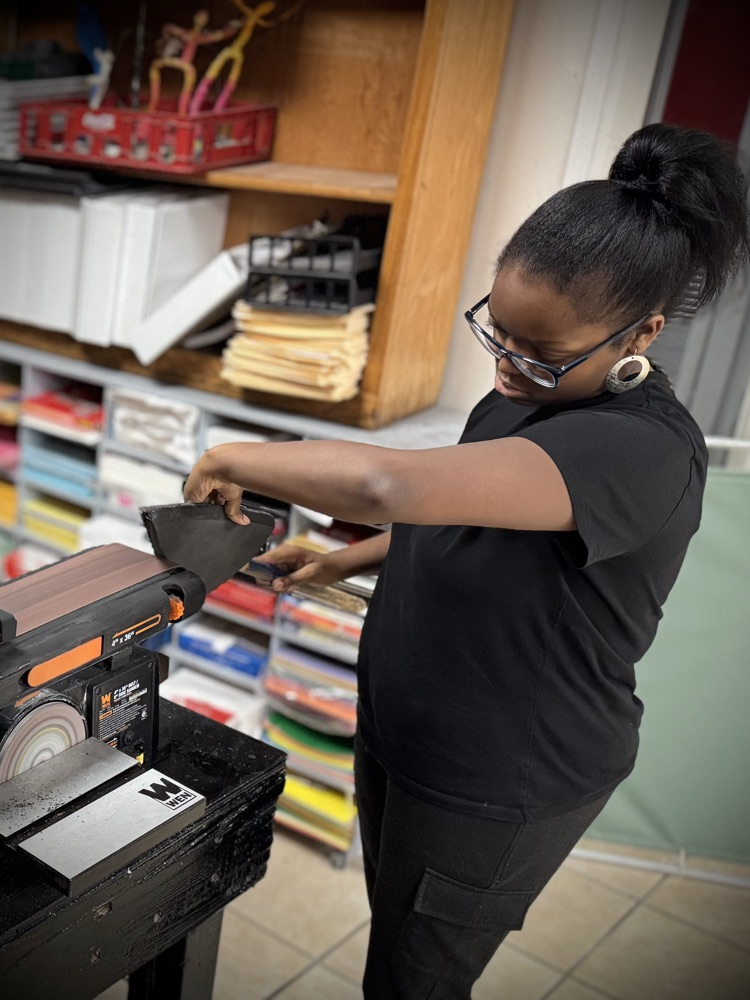 a student files the point of a foam spear on a belt sander