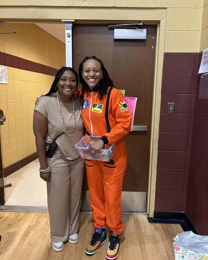Two women stand together and smile for a photo inside a school gym.